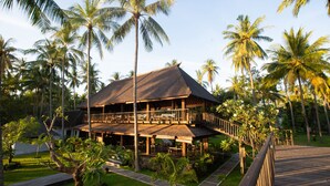 Un resort con una terraza de madera, un área de estar techada al aire libre y palmeras.