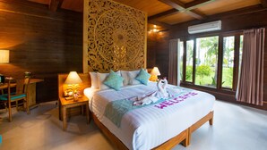 Dormitorio con estructura de madera, una cama grande, dos mesitas de noche con lámparas y vistas a la vegetación a través de amplias ventanas.