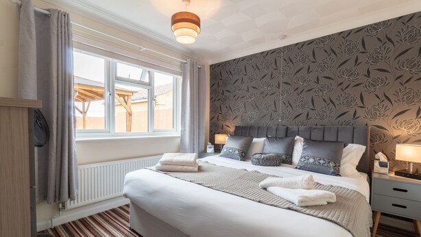 Un lit bien fait, avec une tête de lit grise, une fenêtre avec des rideaux, un radiateur et un mur à motifs.