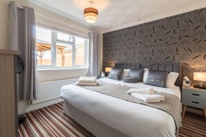 Un lit bien fait, avec une tête de lit grise, une fenêtre avec des rideaux, un radiateur et un mur à motifs.