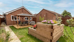 Une maison d’habitation dotée d’un patio, d’un jardin surélevé en bois où sont plantées des fleurs, et d’une façade en briques.