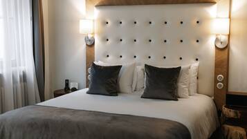 A hotel room with a tufted headboard, two bedside lamps, a bed with a grey blanket, and a nightstand with a remote control.