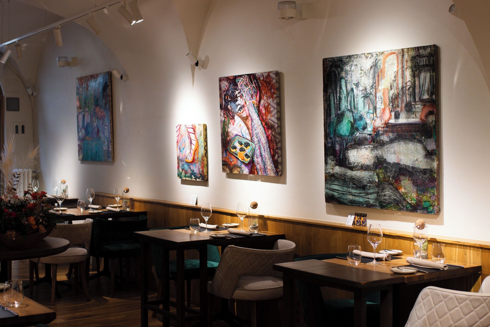 A restaurant interior with tables, chairs, and large abstract paintings on the walls.