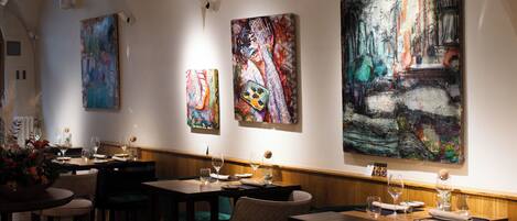 A restaurant interior with tables, chairs, and large abstract paintings on the walls.
