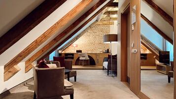 An attic room with a sloped ceiling, exposed wooden beams, a stone wall, a desk, a chair, a sofa, a lamp, and a television.