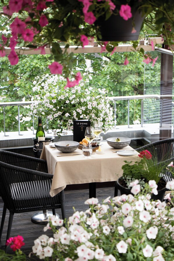 An outdoor dining area with a table set for two, surrounded by potted plants and flowers.