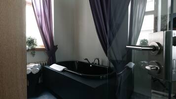 A modern bathroom with a black bathtub, a glass shower enclosure, and a visible towel rack.