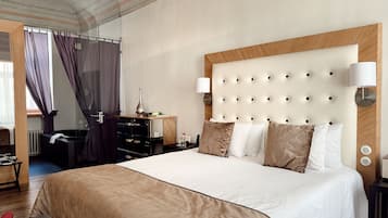 A hotel room with a large bed, a wooden headboard, a bedside table with a lamp, a dresser, and a window with curtains.