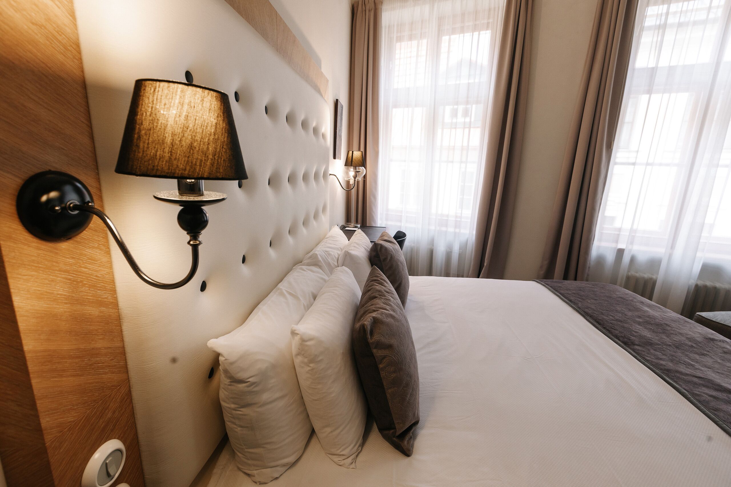 A hotel room with a large bed, a wall-mounted lamp, and a window with curtains.