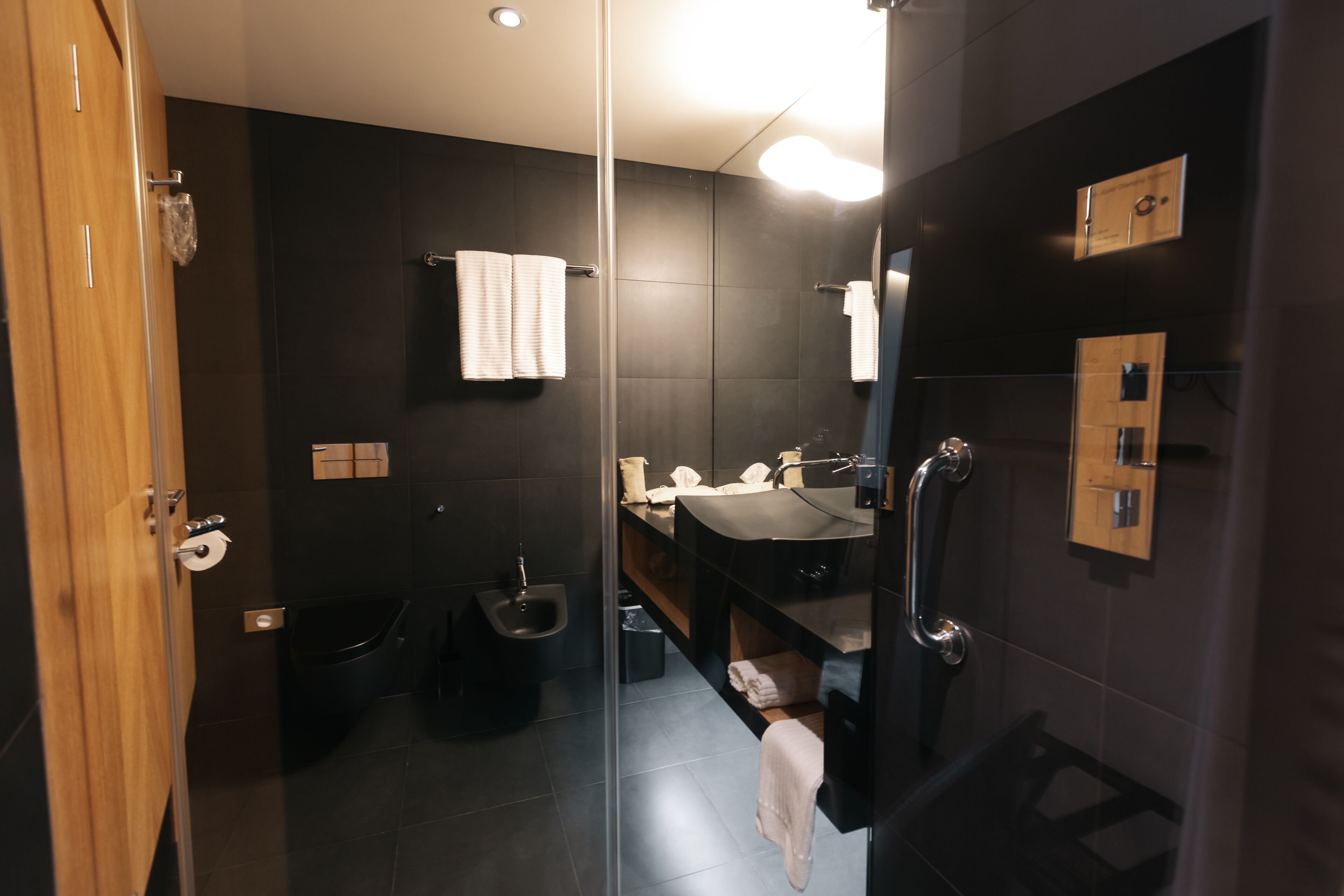 Un baño moderno con cabina de ducha de vidrio, tocador de madera y suelo de baldosas oscuras.
