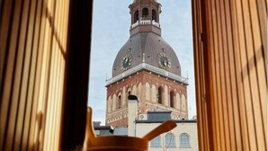 A view through a window of a building with a clock tower and a cup. - Dome Hotel (Riga)