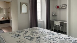 A bedroom with a bed, a desk, and a chair. There is a window with curtains, a mirror, and a shelf with a lamp. - Charming City-Center Apartment with Modern Amenities and Nearby Attractions (Bar-le-Duc)