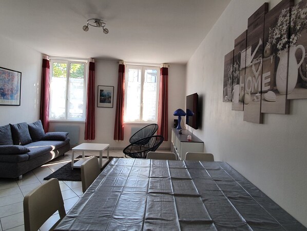 A modern living room with a sofa, dining table, chairs, a TV, and artwork on the walls.