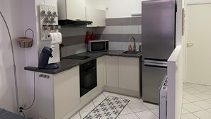 A compact kitchen with a microwave, stove, and refrigerator. There is a small sink and a tiled backsplash. - Charming City-Center Apartment with Modern Amenities and Nearby Attractions (Bar-le-Duc)
