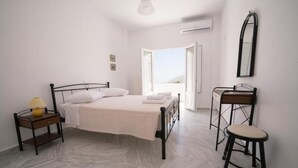 Un dormitorio con cama, mesita de noche, silla y vistas a través de una puerta abierta.