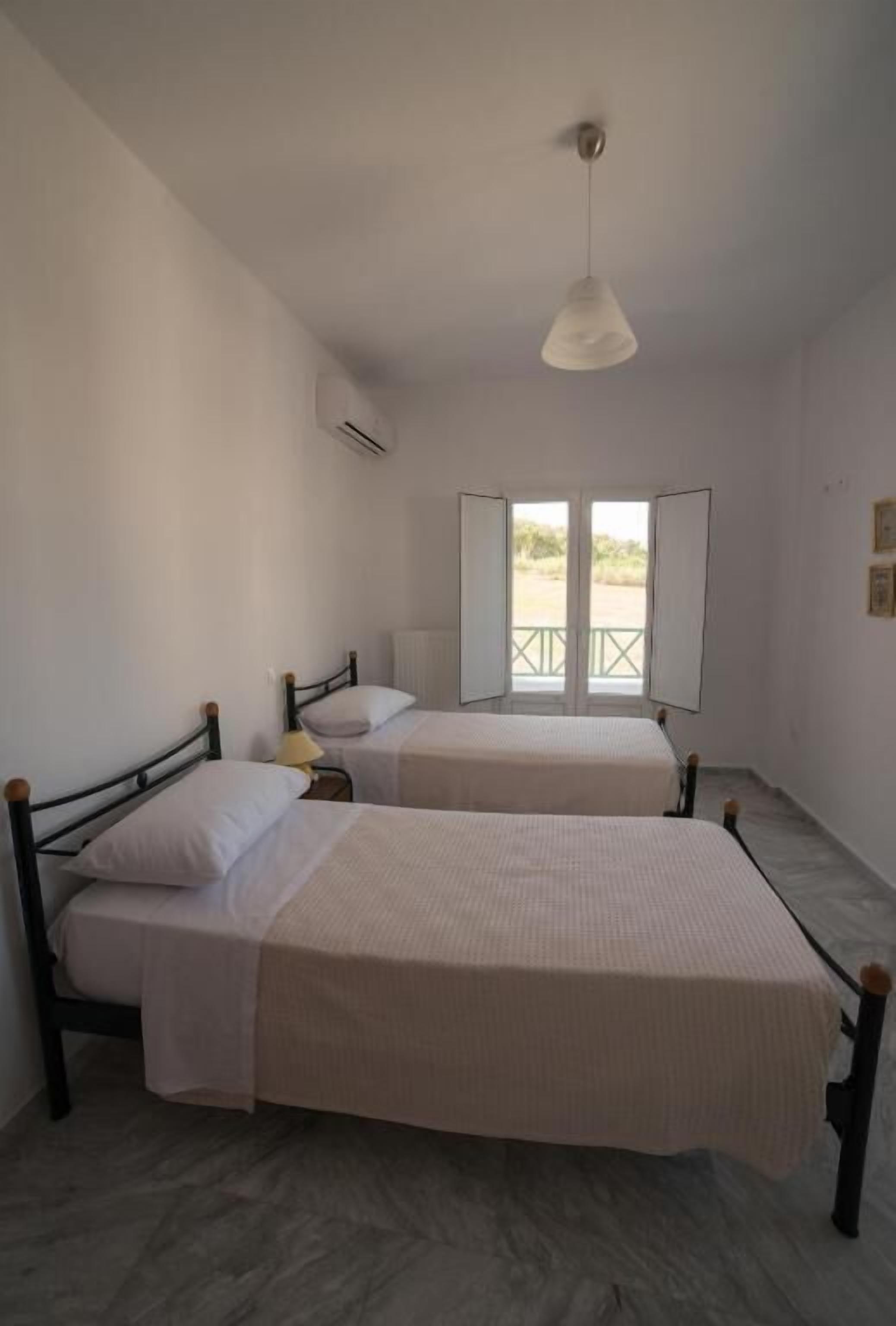 A room with two beds, a ceiling light, and a window with an open door.