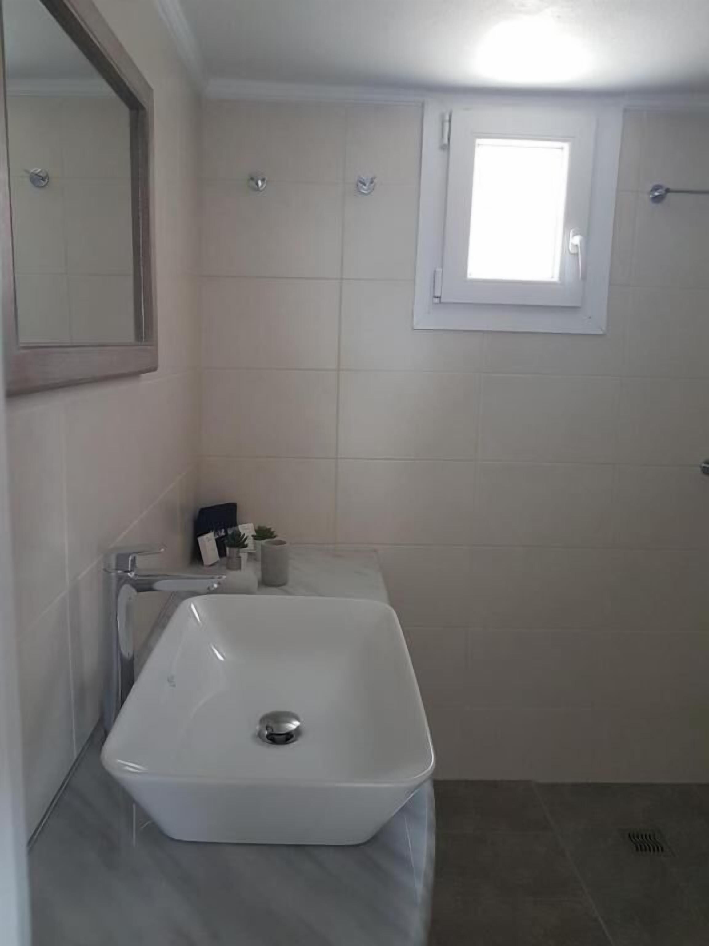 A bathroom with a white sink, a mirror, and a window.
