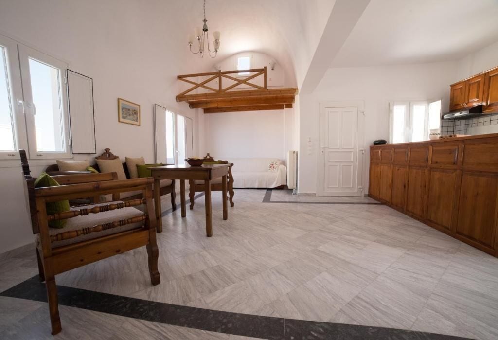 A spacious living area with a wooden dining table and benches, a kitchen with wooden cabinets, and a high ceiling with exposed beams.