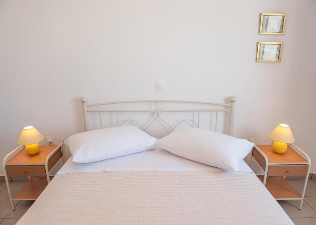 Una cama individual con ropa de cama blanca, dos mesitas de noche con lámparas y dos cuadros en la pared.