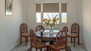 Un comedor con una mesa redonda y seis sillas de madera, un florero con flores y una ventana con persianas.