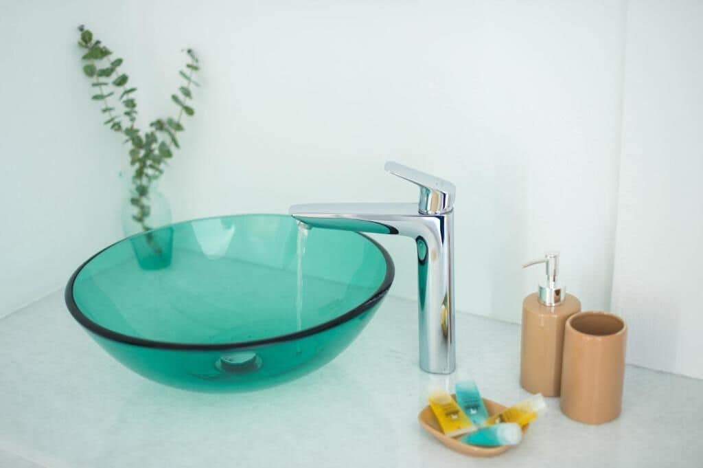 Ein modernes Badezimmer mit einem Waschbecken aus Glas, einem Chromarmaturen und zwei braunen Kosmetikbehältern.