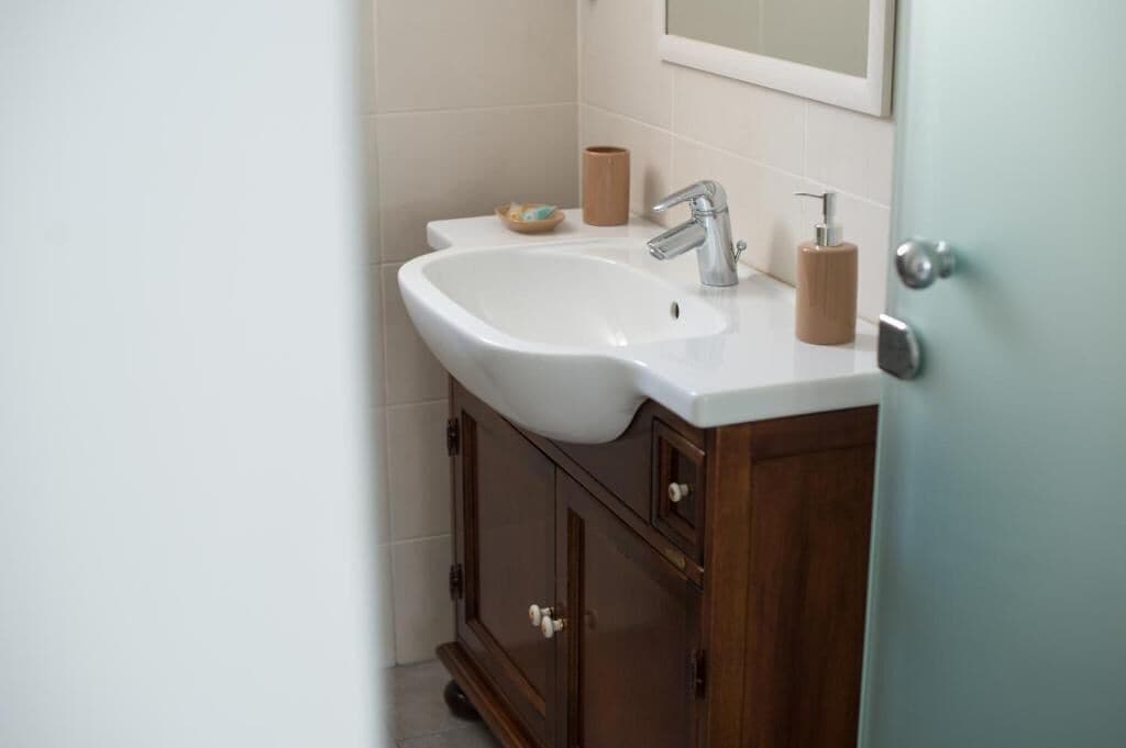 Un baño con un lavamanos blanco, un armario de madera y un espejo sobre el lavamanos.