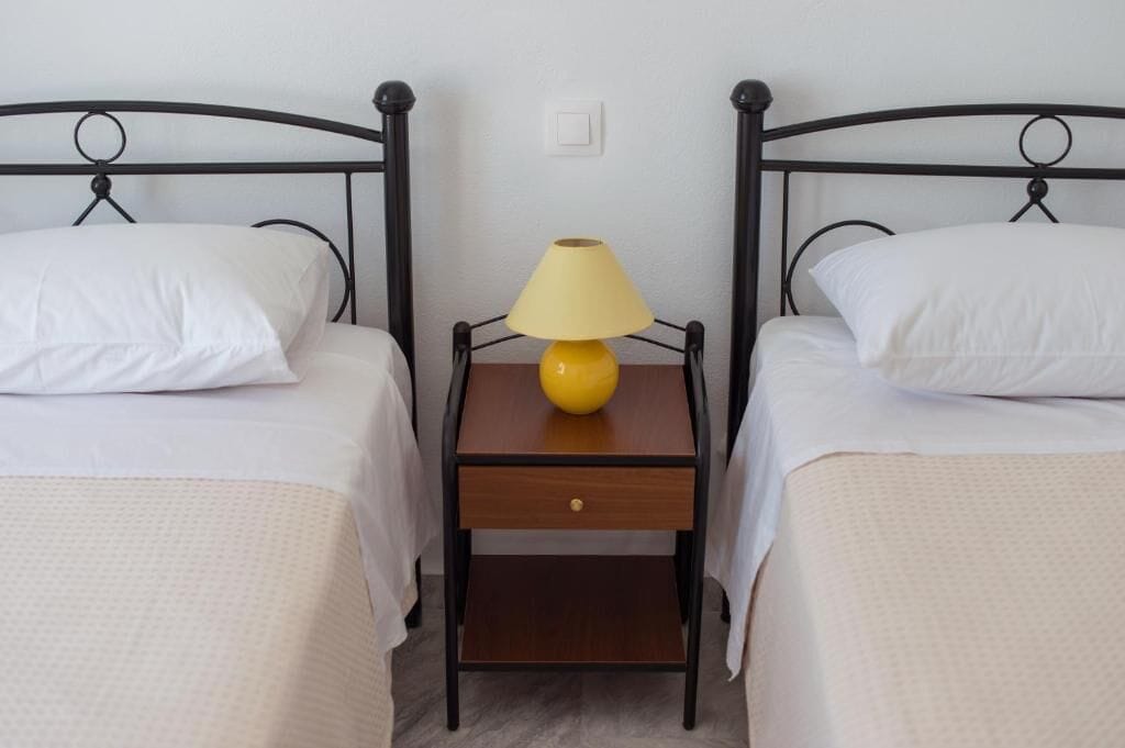 Una habitación con dos camas individuales, cada una con ropa blanca y una mesita de noche de madera entre ellas.