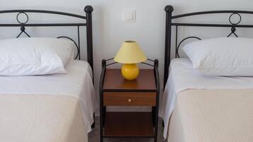 Una habitación con dos camas individuales, cada una con ropa blanca y una mesita de noche de madera entre ellas.