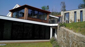 A modern house with a large glass facade, a wooden deck, and a stone retaining wall.