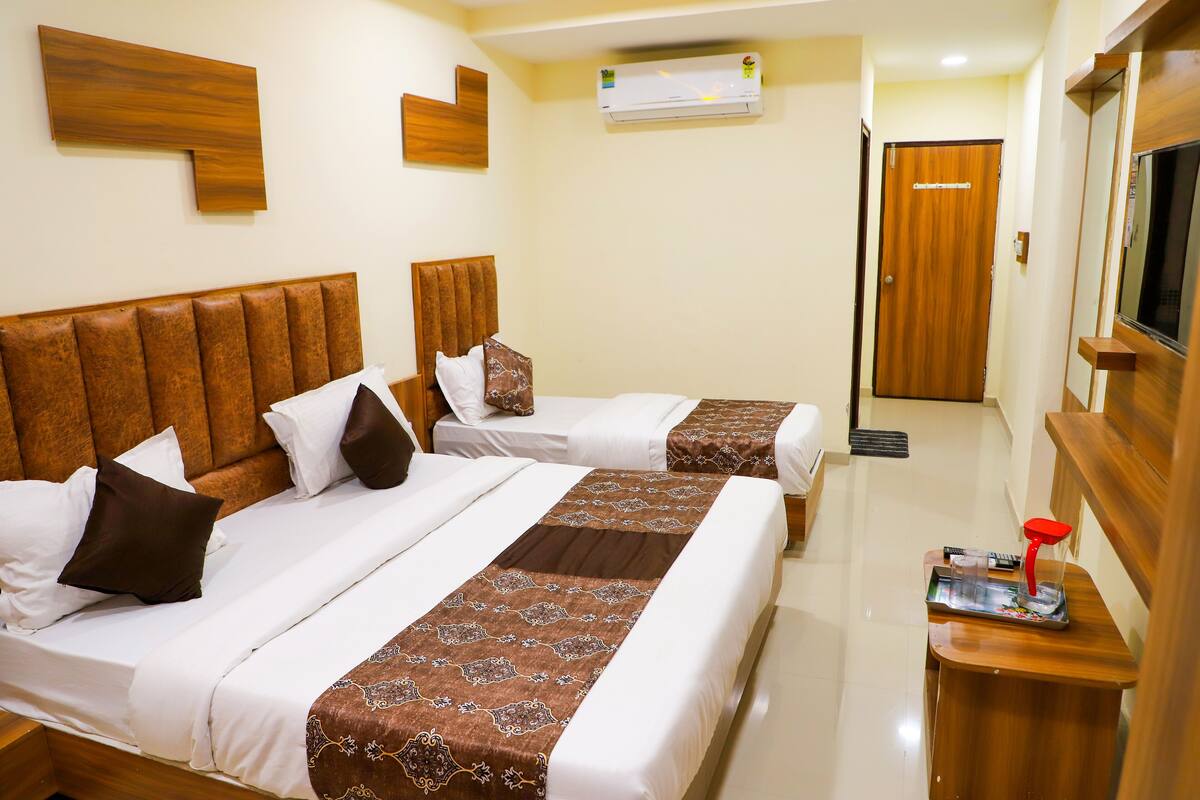 Two beds with headboards, white bedding, brown decorative pillows, and a wooden nightstand with a red object.