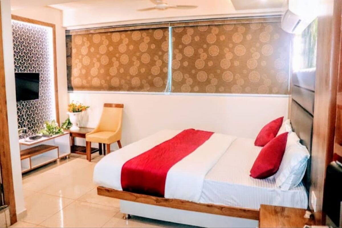 A modern hotel room with a large bed, a desk, a chair, and a TV.