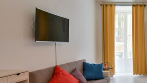 A living room with a flat-screen TV mounted on the wall, a sofa with colorful cushions, a wooden coffee table, and a sliding glass door leading to an outdoor area. - Tasso Apartment - between History and the Coast - (Salerno)