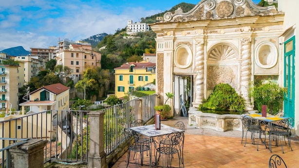 A terrace with a table and chairs, a decorative archway, and a view of surrounding buildings. - Tasso Apartment - between History and the Coast - (Salerno)
