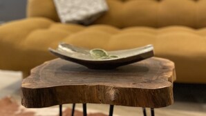 Ein Holztisch mit einer Schüssel darauf, vor einer Couch mit Kissen platziert.