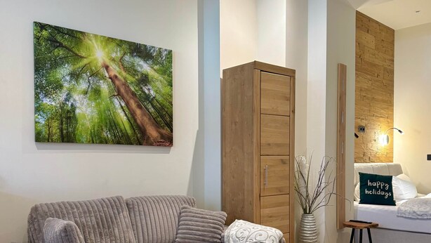 Ein modernes Wohnzimmer mit einem Ecksofa, einem kleinen Hocker, einer Holzkommode und einem Wandbild.