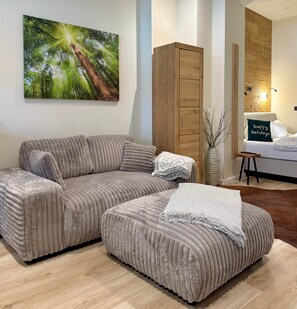 Ein modernes Wohnzimmer mit einem Ecksofa, einem kleinen Hocker, einer Holzkommode und einem Wandbild.
