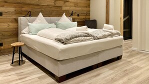 Un dormitorio moderno con cabecera de madera, un taburete pequeño de madera y una cama bien hecha con almohadas y una colcha.