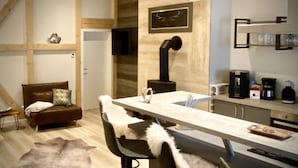 Una cocina moderna con una isla central, un comedor con mesa y sillas blancas, un sofá con cojines estampados y una chimenea.