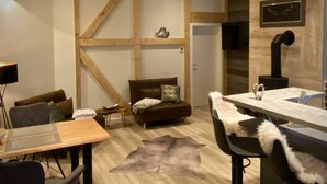 Una sala moderna con techo de madera, un sofá de cuero marrón, una mesa de comedor de vidrio y un plaid de piel.