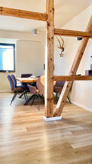 A dining area with a wooden ceiling structure, a table with chairs, and a decorative antler on the wall.