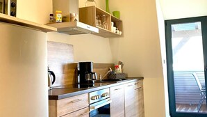 A modern kitchen with wooden cabinets, a built-in oven, a coffee maker, and a window overlooking a deck. - App. 4 - wohlBleben (4 Zi, 6 Pers.) (Braunlage)