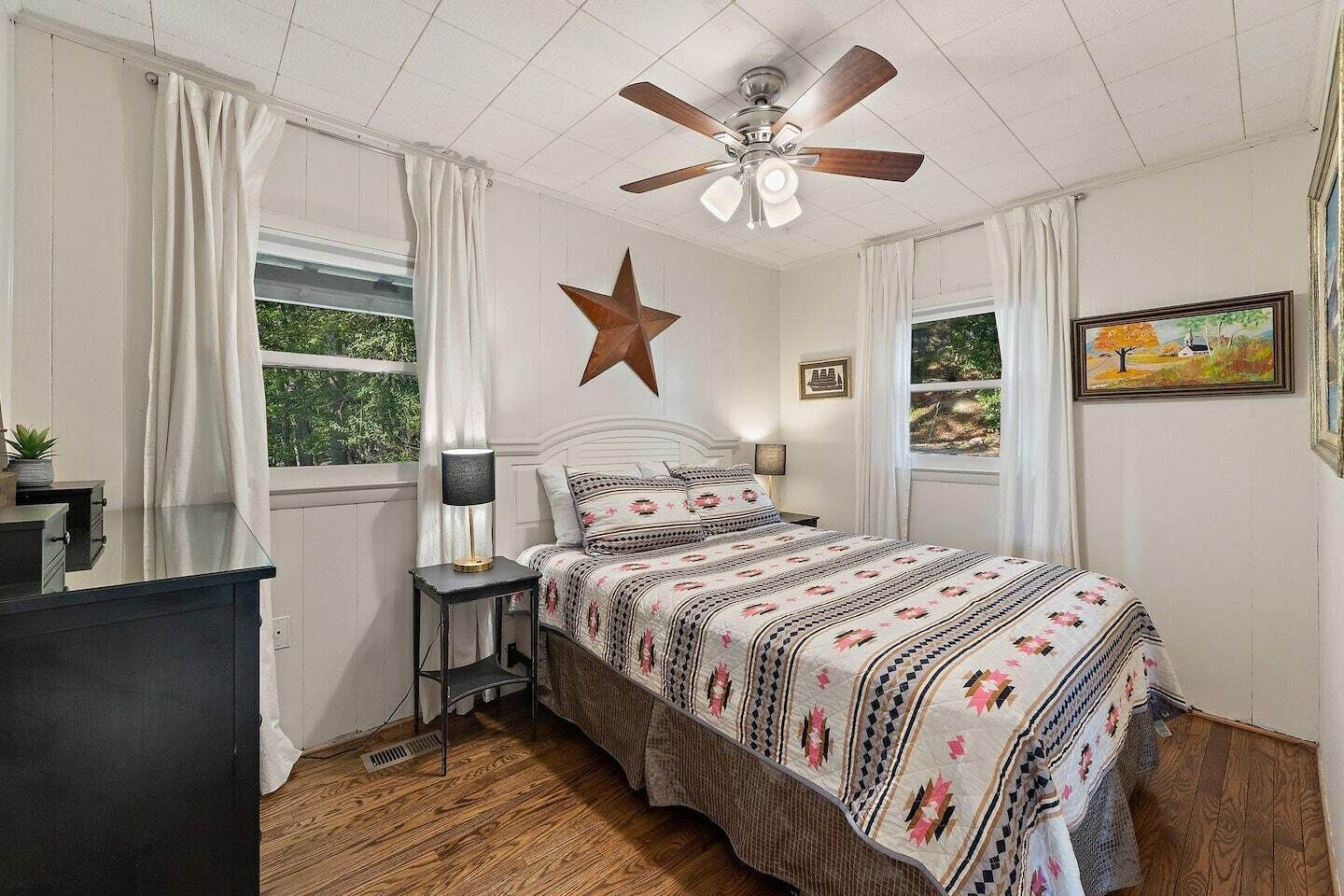 Un dormitorio con cama, decoración de estrellas, ventilador de techo y ventana con cortinas.