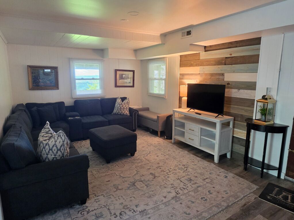 Ein Wohnzimmer mit Ecksofa, Hocker, TV-Möbel und einem gemusterten Teppich.