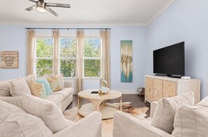 A living room with a sofa, a coffee table, a television, and a painting on the wall. - Blue Haven by the Sea - 3BR/2.5BA Blue Mountain Beach - Sleeps 8 - Community Pool (Santa Rosa Beach)