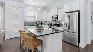 Una cocina moderna con gabinetes blancos, electrodomésticos de acero inoxidable y una isla central con taburetes de bar.