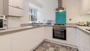 A modern kitchen with white cabinets, a gas stove, a microwave, and a toaster. - 3 South Beach Court - Cosy Seafront Apartment (Tenby)