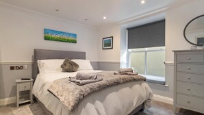 A bedroom with a bed, a nightstand, a dresser, a window with a view, and a painting on the wall. - 3 South Beach Court - Cosy Seafront Apartment (Tenby)