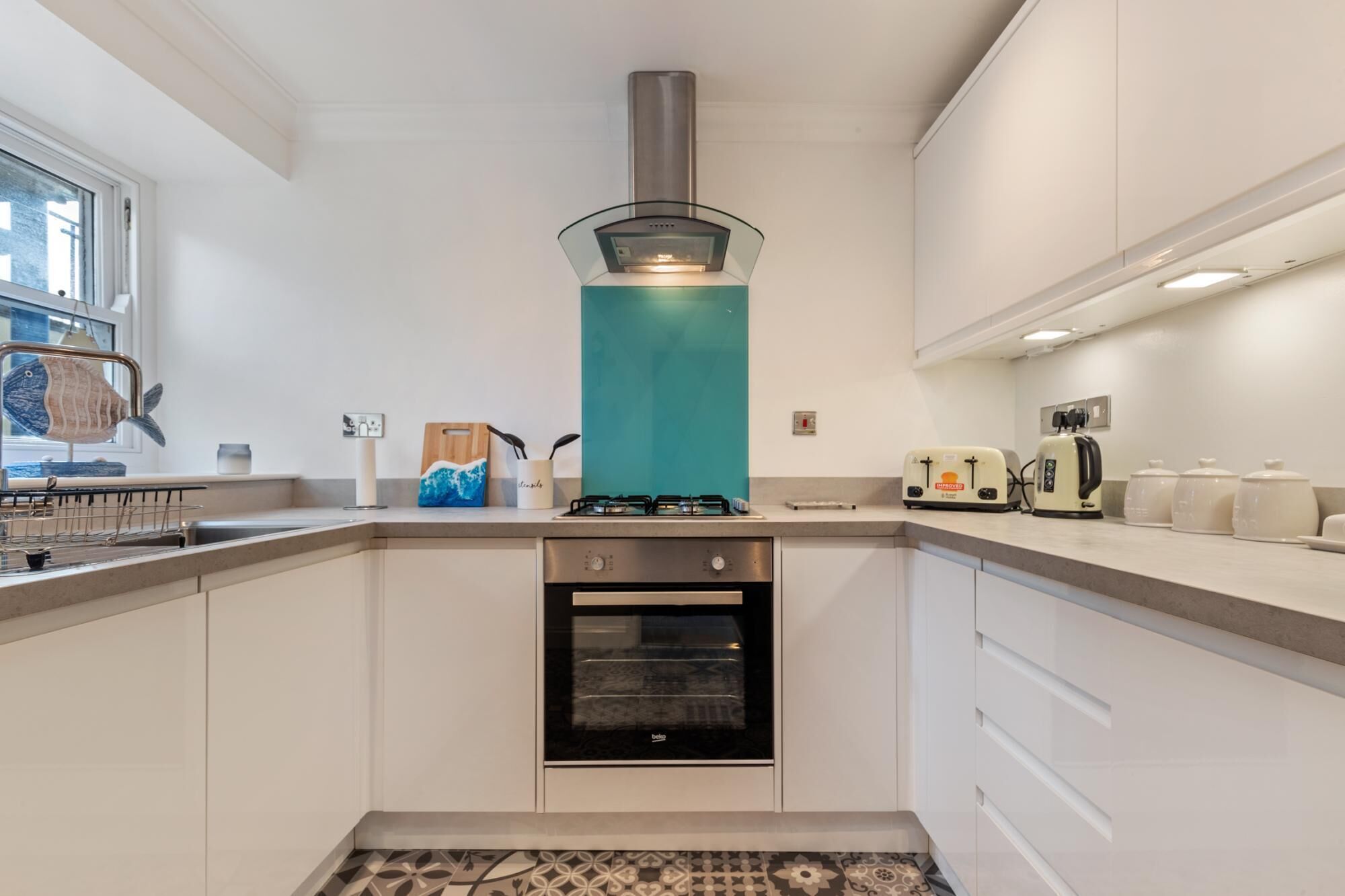A modern kitchen with white cabinets, a stainless steel range hood, a built-in oven, a toaster, and a coffee maker.
