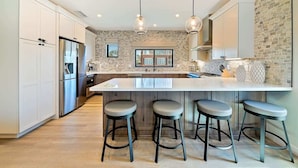 A modern kitchen with a large island, bar stools, and pendant lighting.