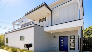 A modern two-story house with a flat roof, a blue door, and a mailbox.